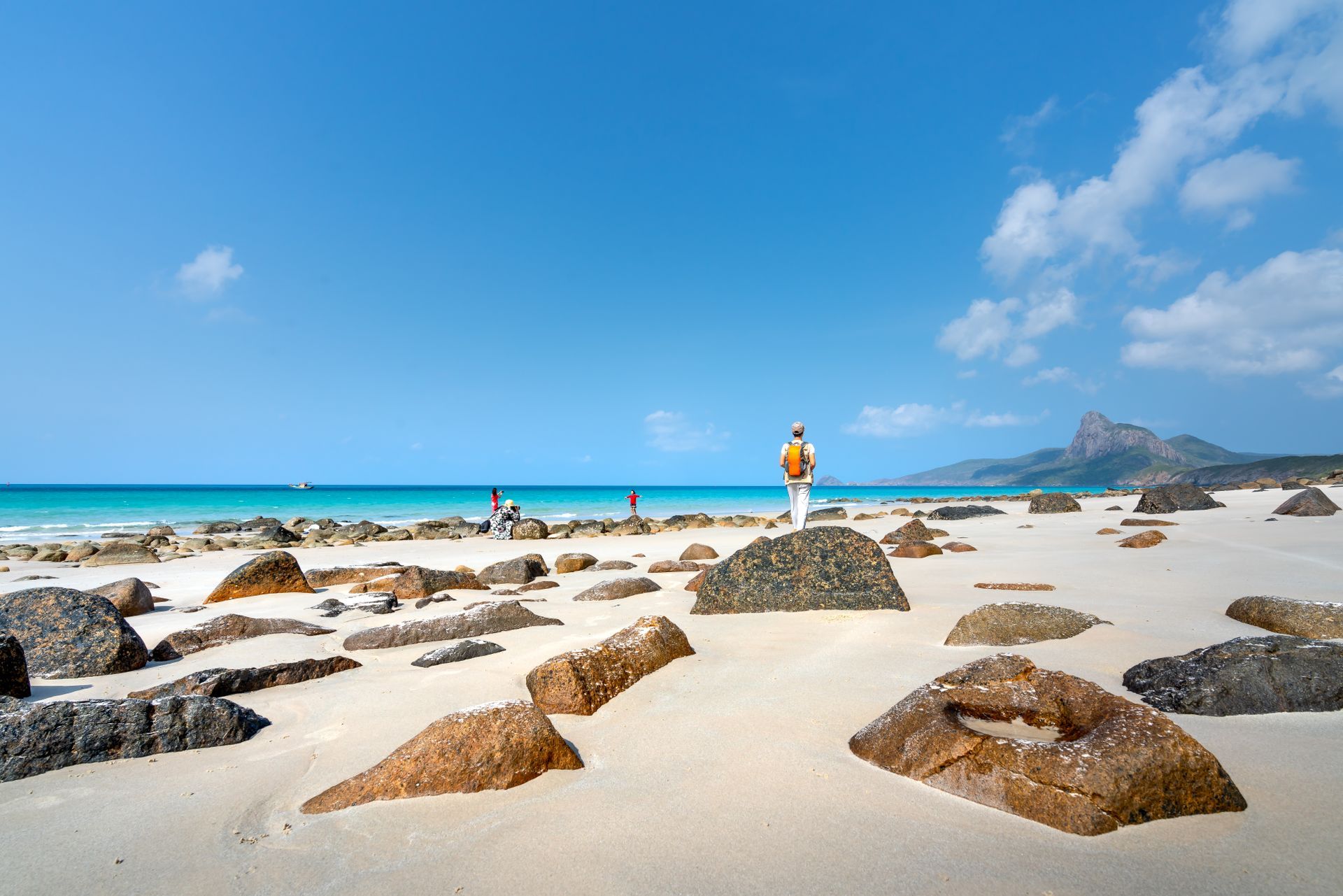 Traveler walking on a white sand beach scattered with boulders on the northeast coast of Socotra
