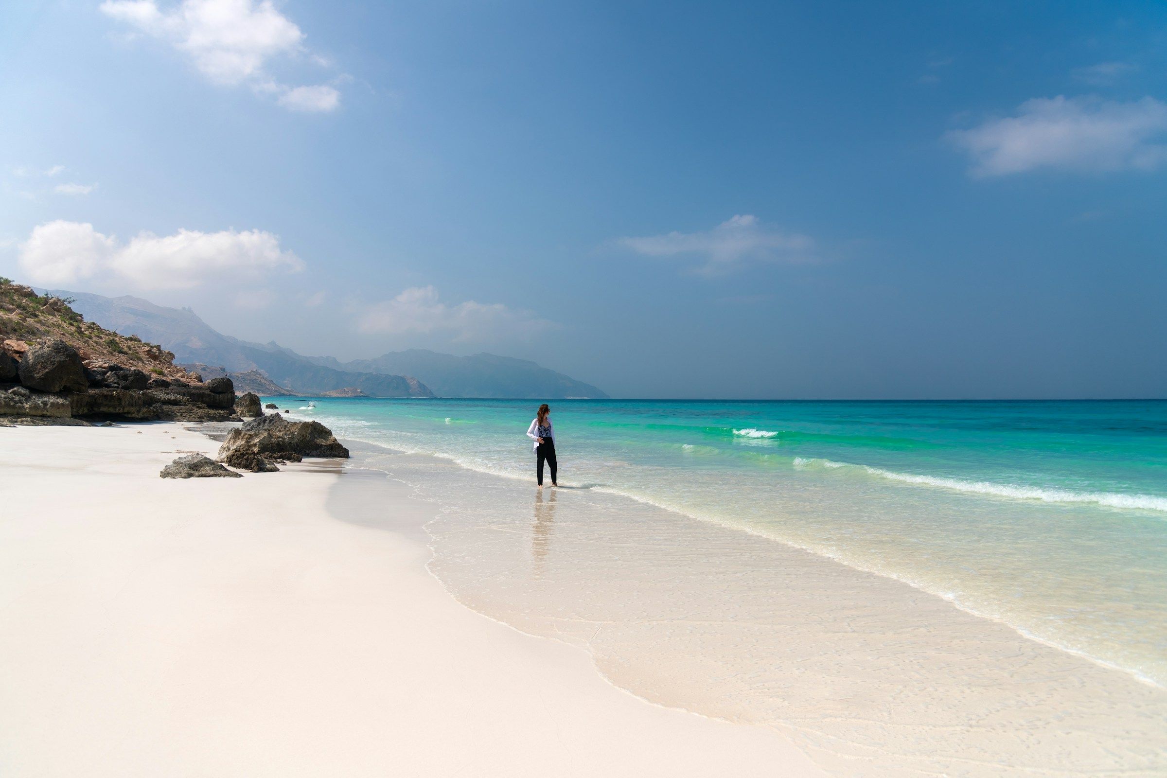 Lone traveler standing in shallow turquoise water on the remote white sand of Shoab Beach
